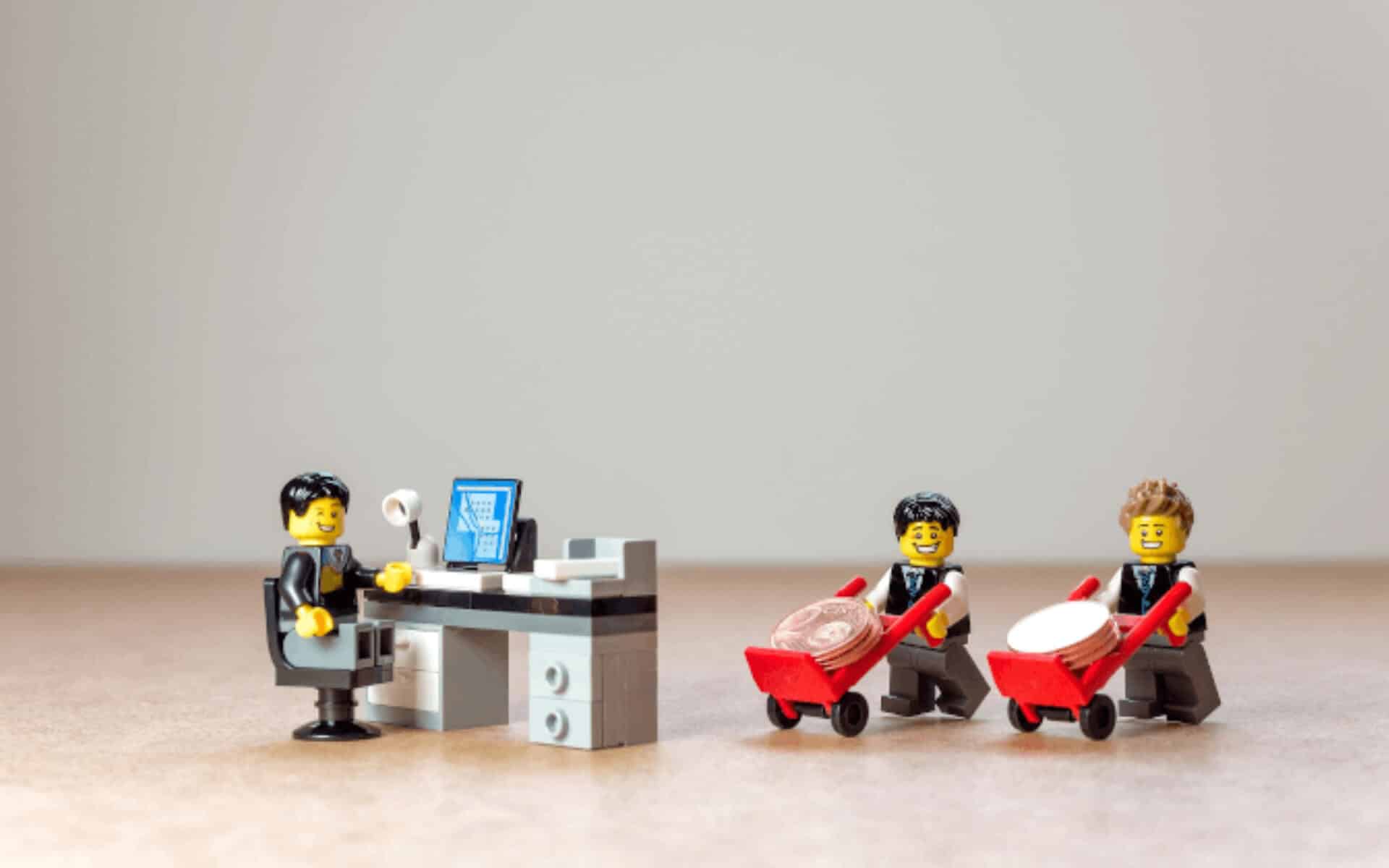 Lego workers grin pushing carts full of coins to a happy boss